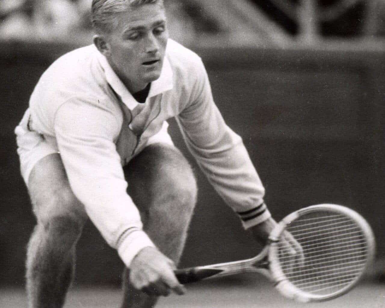 Lew Hoad crouching low to play a backhand on a grass court at Kooyong in 1954